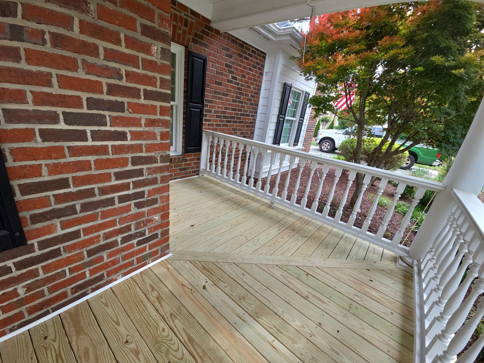 Wood porch deck with white railings on a brick home